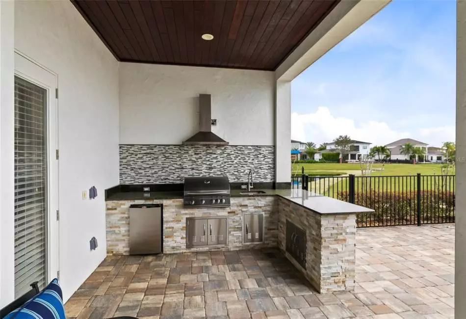 Outdoor entertaining is a breeze with a summer kitchen featuring a grill, sink, fridge, and bar seating.