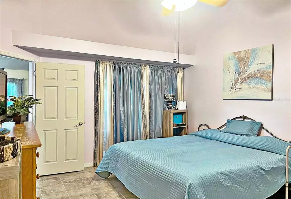 Master bedroom with sliding glass doors onto enclosed rear lanai, ceramic tile flooring, decorative shelves